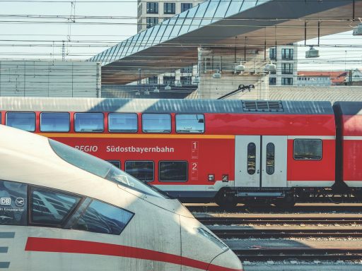 Zwei Züge an einem Bahnhof, einer rot und einer in grauen Farben.